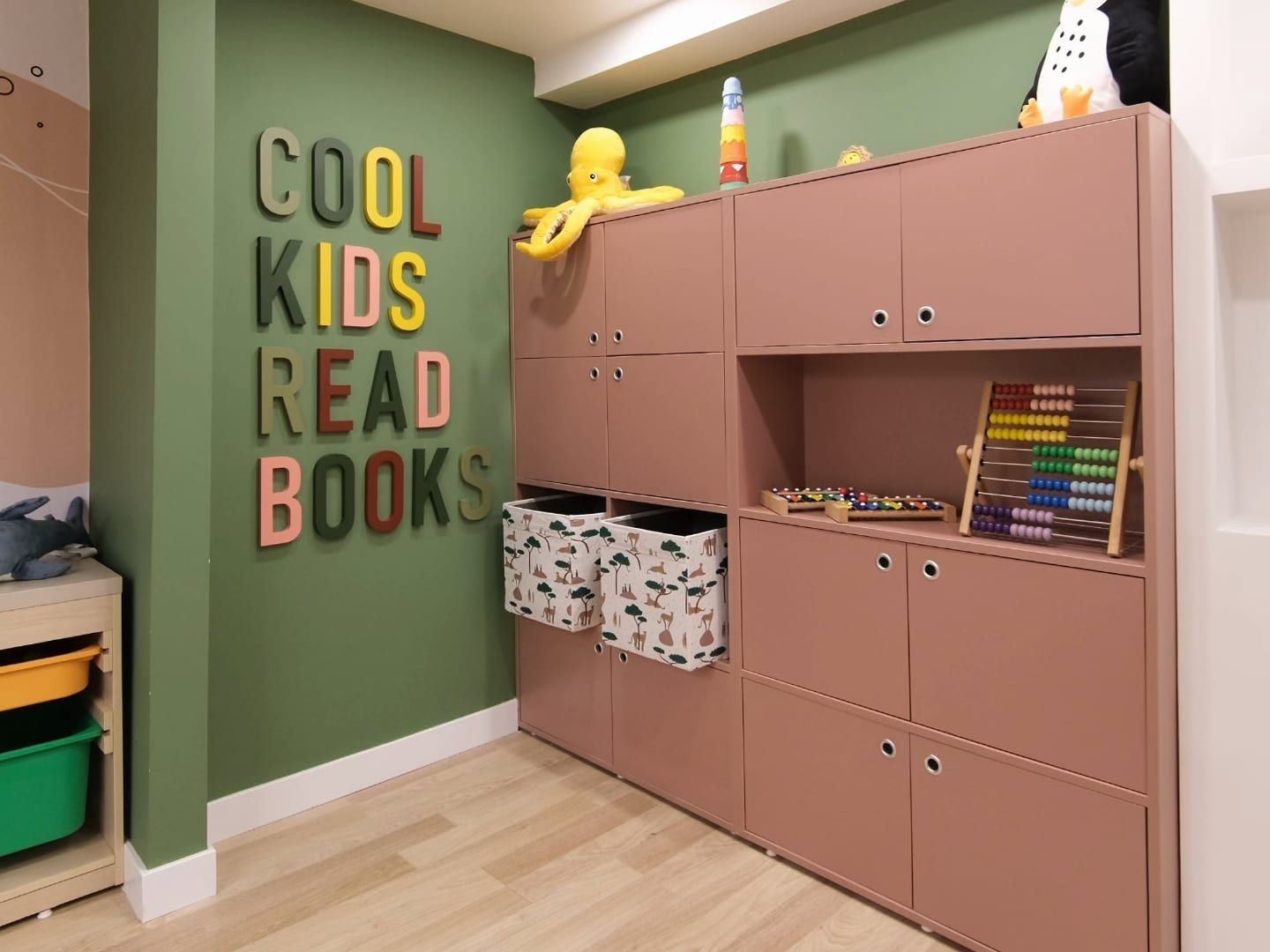 Renkli harflerle "COOL KIDS READ BOOKS" yazılı yeşil duvarlı okuma köşesi