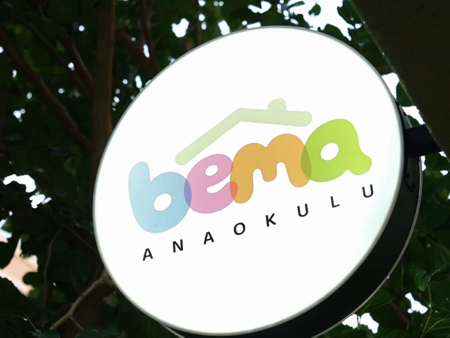 Akşam ağaç yaprakları arasında ışıklı BEMA Anaokulu tabelası